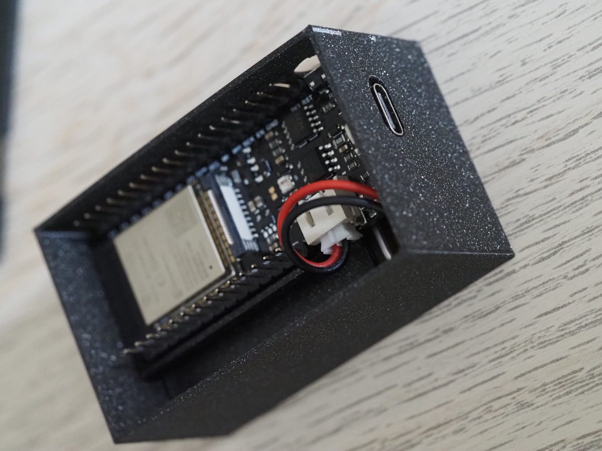 The FireBeetle and its battery lead sitting in the black 3D-printed case, with the USB-C port lined up with a slot in the end.